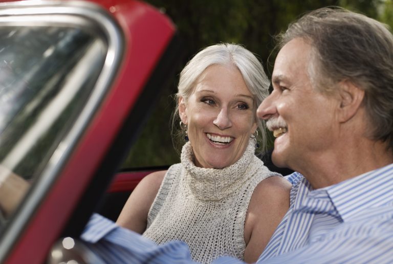 senior couple driving red convertible