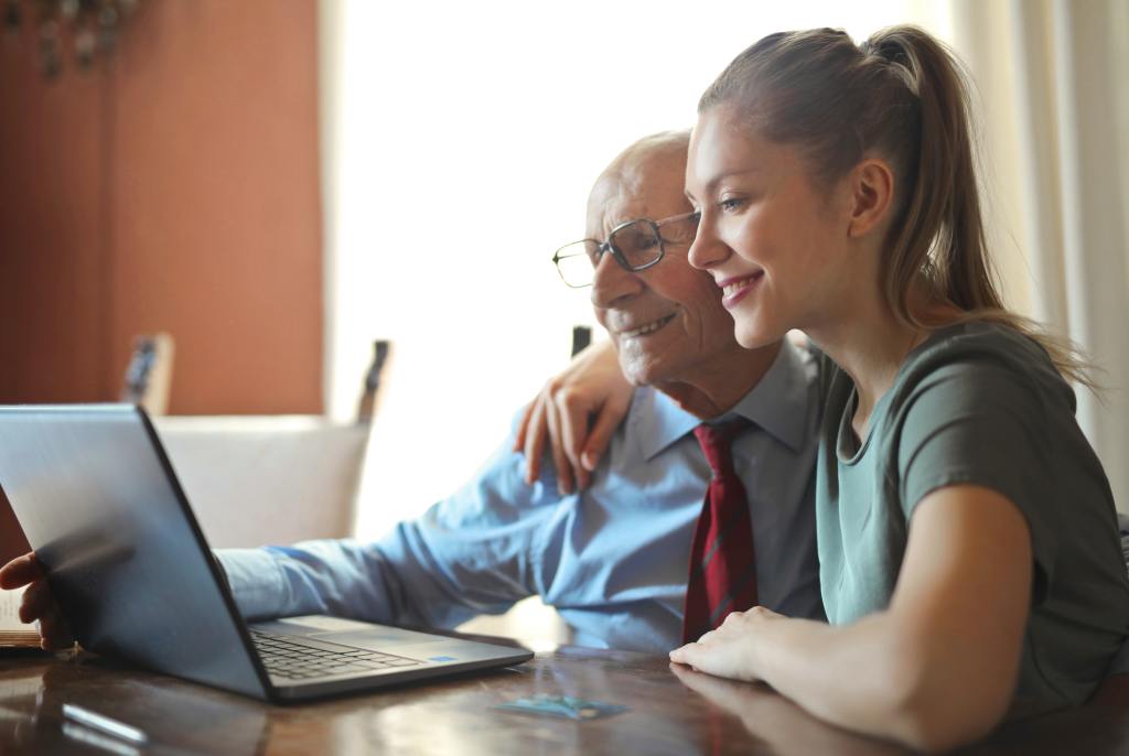 smiling woman helping senior man use computer
